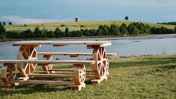 A picnic table set on a grassy area near a body of water with a distant view of a hill and a silo.