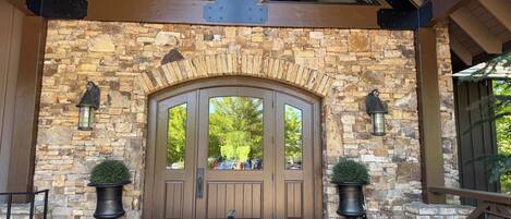 A stone entrance with a wooden door, two potted plants, and a stone floor.