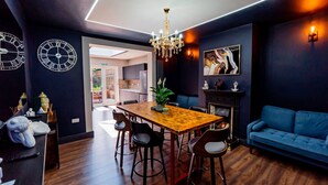 A modern dining area with a wooden table, black chairs, a chandelier, and a blue sofa. - London Heathrow Airport 6 Bedroom Ensuite (West Drayton)