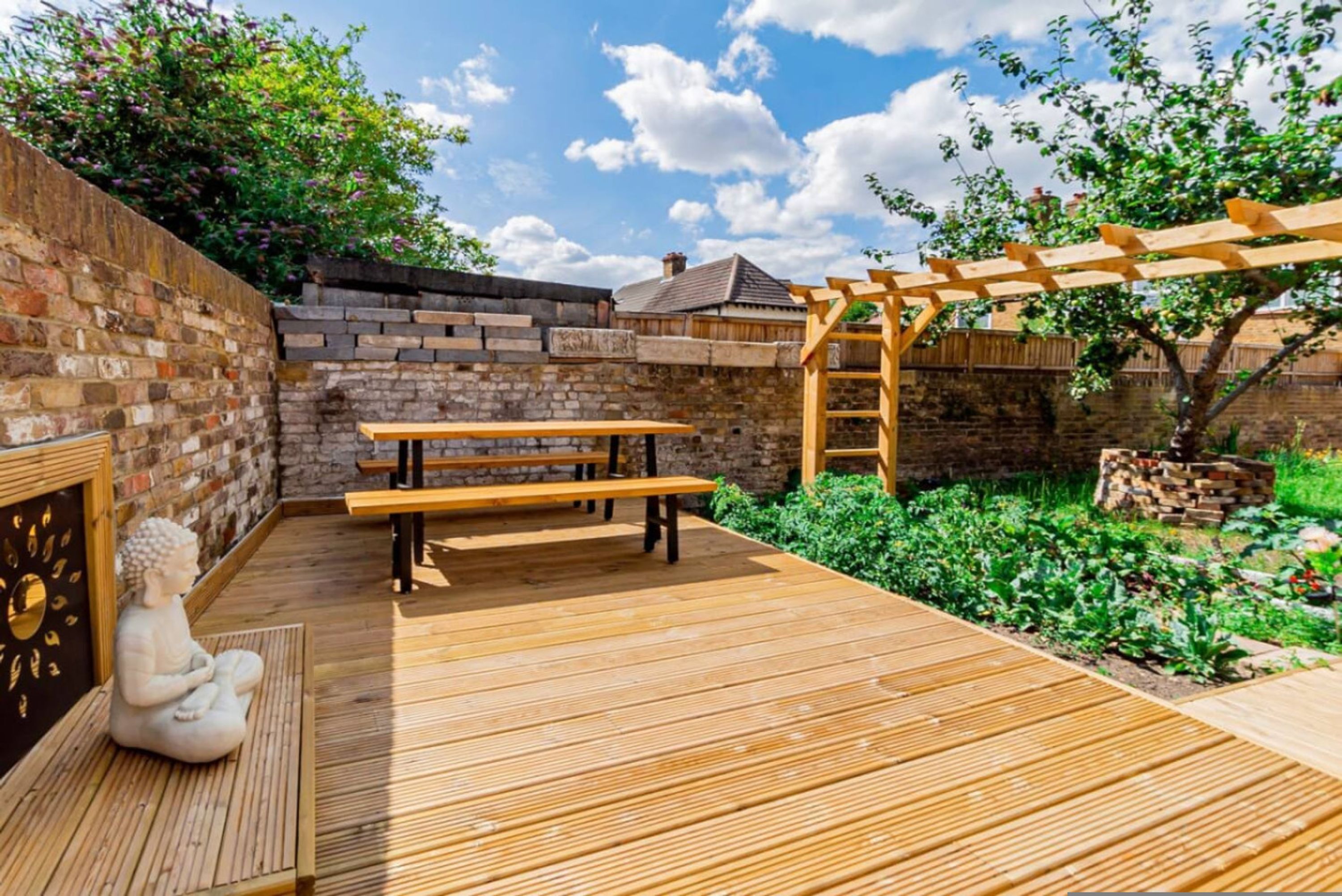 A wooden deck with benches, a statue, and a pergola.