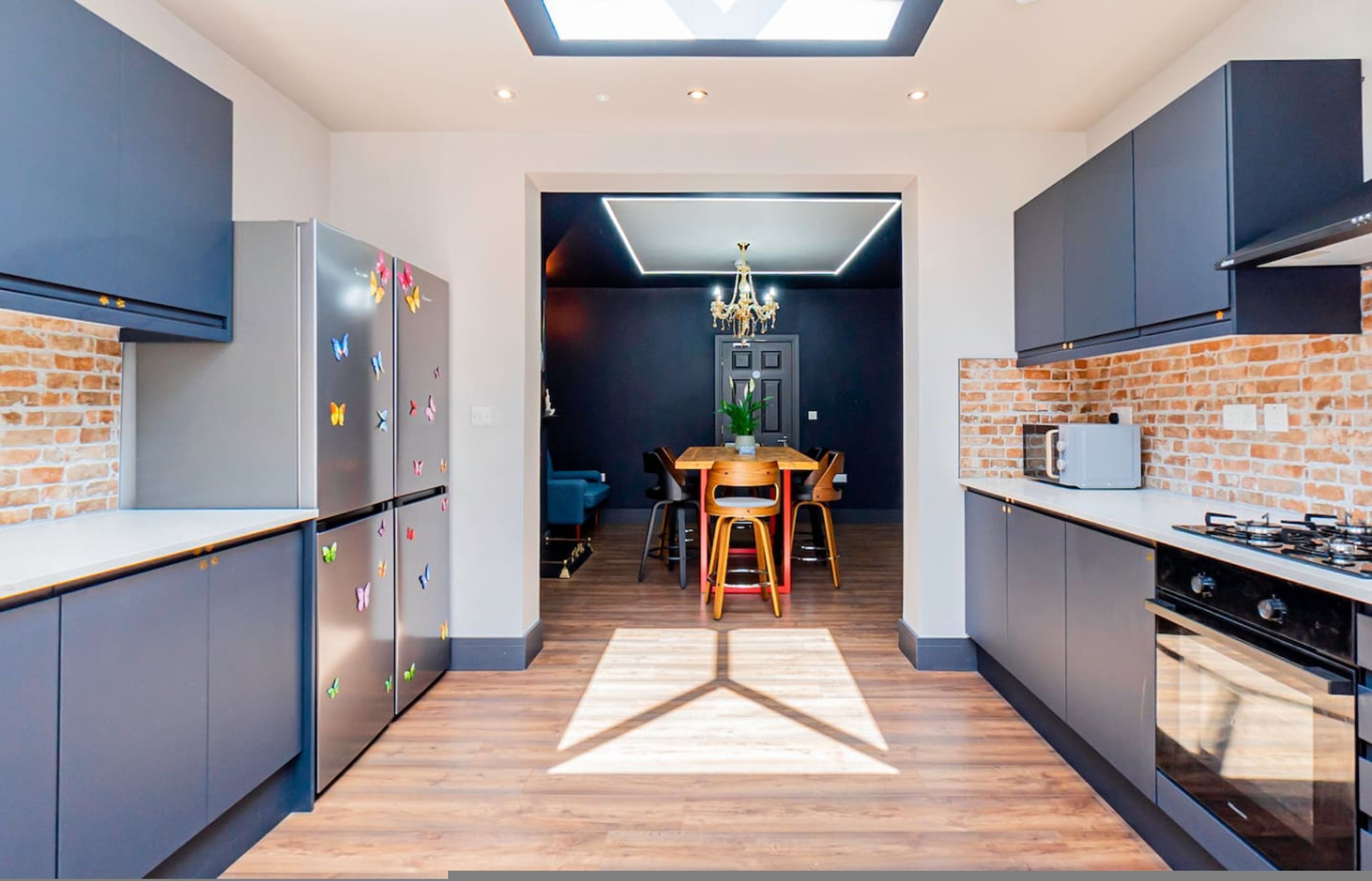 A modern kitchen with a brick wall, a dining area with a chandelier, and a skylight.