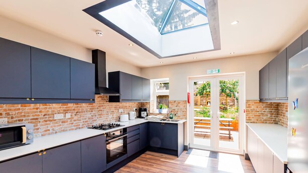 A modern kitchen with dark cabinets, a skylight, and a view of the outdoors. - London Heathrow Airport 6 Bedroom Ensuite (West Drayton)