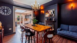 A modern dining area with a wooden table, black chairs, a chandelier, and a blue sofa. - London Heathrow Airport 6 Bedroom Ensuite (West Drayton)