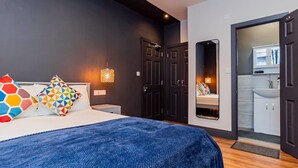 A bedroom with a bed, a nightstand, a dresser, a mirror, and a bathroom visible through an open door. - London Heathrow Airport 6 Bedroom Ensuite (West Drayton)