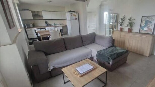 Un espacio habitable pequeño con un sofá, una mesita, un armario y una kitchenette al fondo.