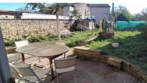 Un patio con una mesa redonda y sillas, un muro de piedra y una zona ajardinada con cerramiento.