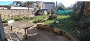 Une terrasse avec une table ronde et des chaises, un mur en pierre et une pelouse délimitée par une clôture.