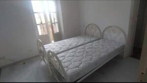 Una cama individual con un colchón acolchado en una habitación con paredes blancas y un ventanal.