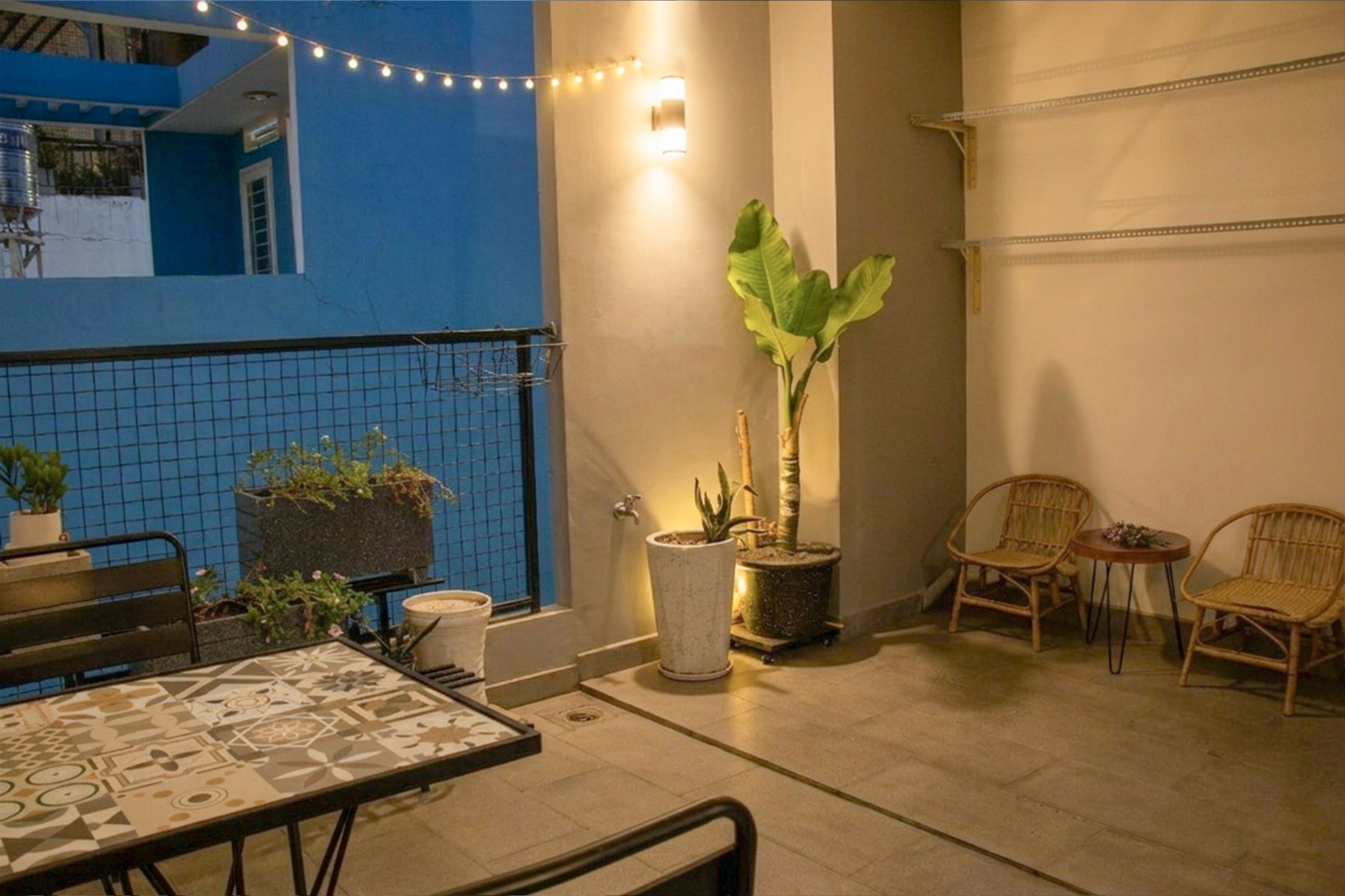 Uma varanda com mesa, cadeiras, plantas em vasos e luzes de festa.
