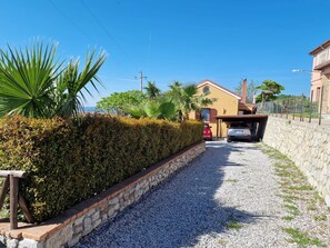 Una strada sterrata che conduce a una casa, con un muro in pietra su un lato e un siepe sull'altro.