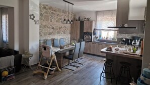 A modern kitchen with a stone wall, wooden cabinets, a dining area with a high chair, and a bar area with stools. - 🦋the village villa 🦋 (Santa Caterina dello Ionio)