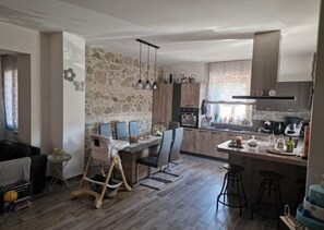 Eine moderne Küche mit Steinwand, Holzschränken, einem Essbereich mit Hochstuhl und einer Bar mit Barhocker.