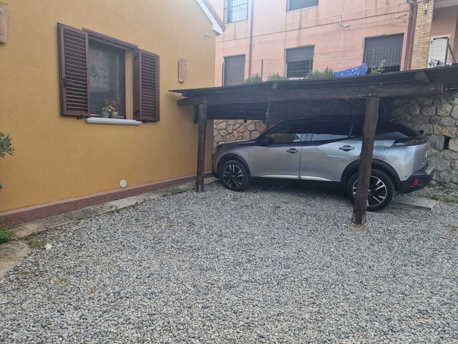 Un VUS argenté était garé sous une pergola en bois, sur une allée recouverte de gravier.