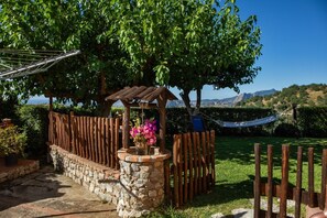 A garden with a wooden pergola, a hammock, and a stone wall.