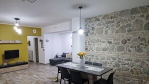 A dining area with a stone wall, a table with chairs, a vase with flowers, and a television on a stand. - 🦋the village villa 🦋 (Santa Caterina dello Ionio)