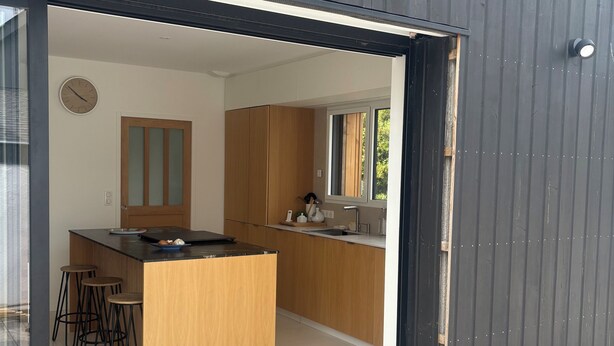 Eine moderne Küche mit Holzschränken, einer zentralen Kochinsel mit Barhocker und einem großen Fenster.