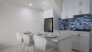 Een moderne keuken met witte kasten, een roestvrijstalen koelkast, een blauwe tegelachtergrond en een klein eiland met barkrukken.