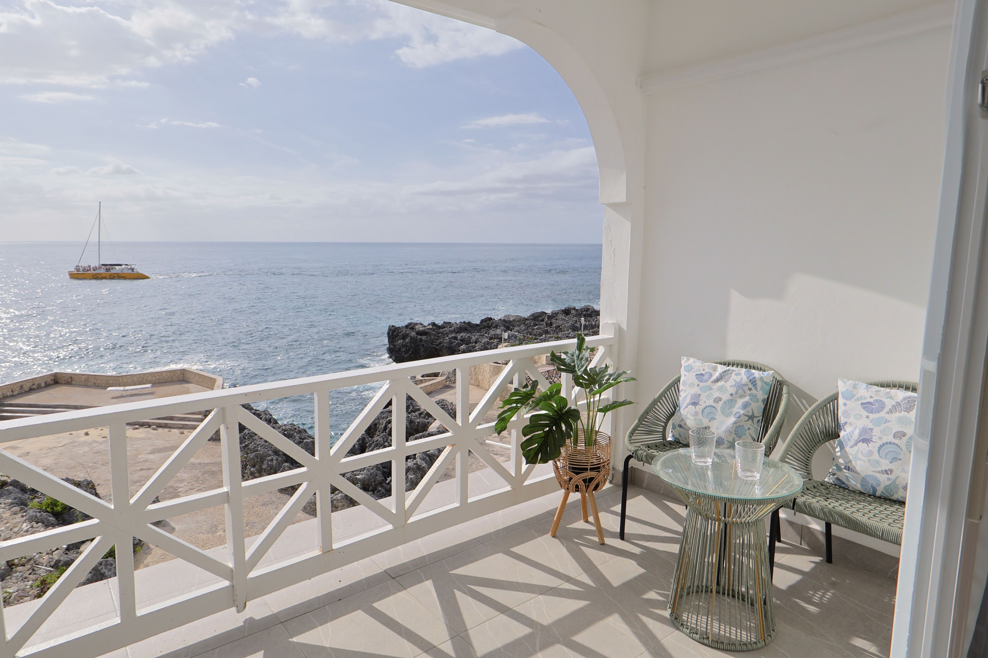 Un balcone con vista sul mare, un tavolino in vimini con sedie e una pianta in vaso.