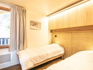 Een slaapkamer met twee eenpersoonsbedden, een houten hoofdbord, een klein nachtkastje en een raam met gordijnen.