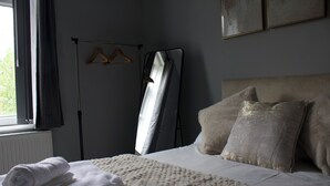 Un lit bien fait, avec une serviette blanche roulée, un portant à vêtements et un grand miroir.