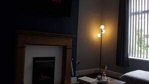 Une pièce avec une cheminée, un téléviseur fixé au mur qui affiche « NETFLIX », et un lampadaire.