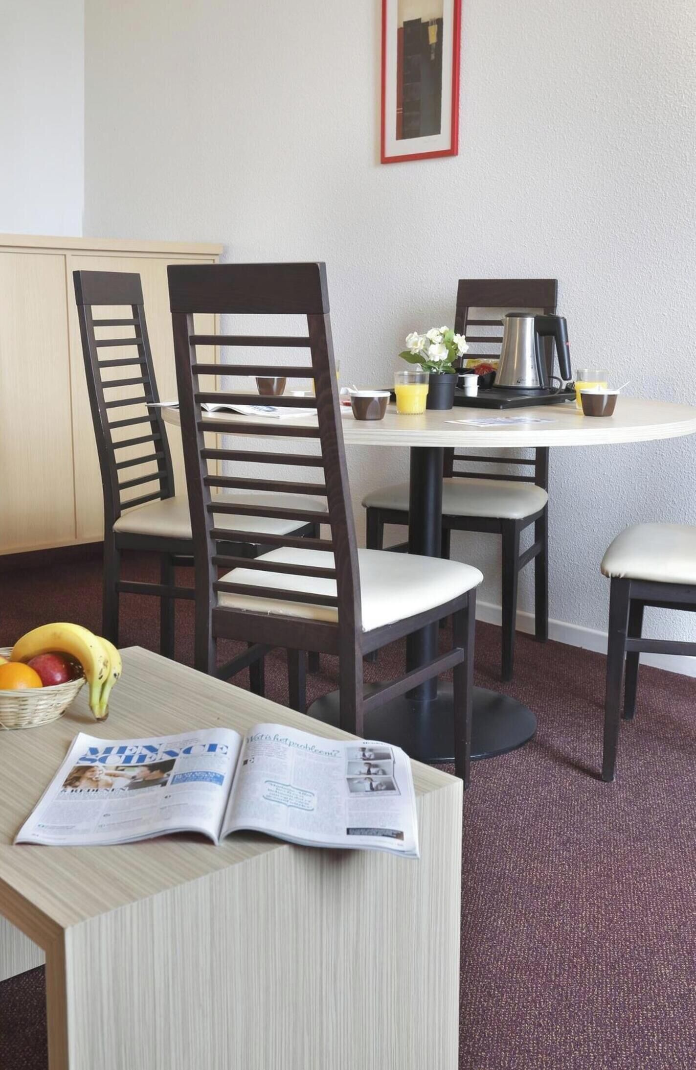 A dining area with a table, chairs, a coffee maker, a framed picture, and a magazine on the table.
