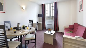 A compact room with a dining table, chairs, a small sofa, a TV, and a window with curtains. - Elegant Vineyard Stay for Three (Epernay)