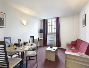 A compact room with a dining table, chairs, a small sofa, a TV, and a window with curtains. - Elegant Vineyard Stay for Three (Epernay)
