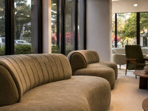 A modern interior with a sofa and a chair, large windows, and a view of the outside. - Hotel Plaza Belmar by HCC (Campo Grande)