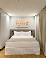 A modern hotel room with a large bed, a wall-mounted abstract painting, and a curtain on the window.