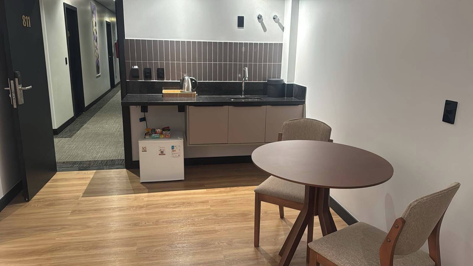 A compact kitchen with a sink, a small refrigerator, and a round dining table with chairs.