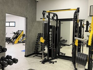 Un gimnasio con equipamiento de levantamiento de pesas, un espejo y una puerta que da a otra habitación.