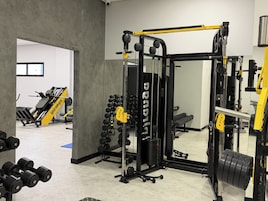 A gym with weightlifting equipment, a mirror, and a door leading to another room.
