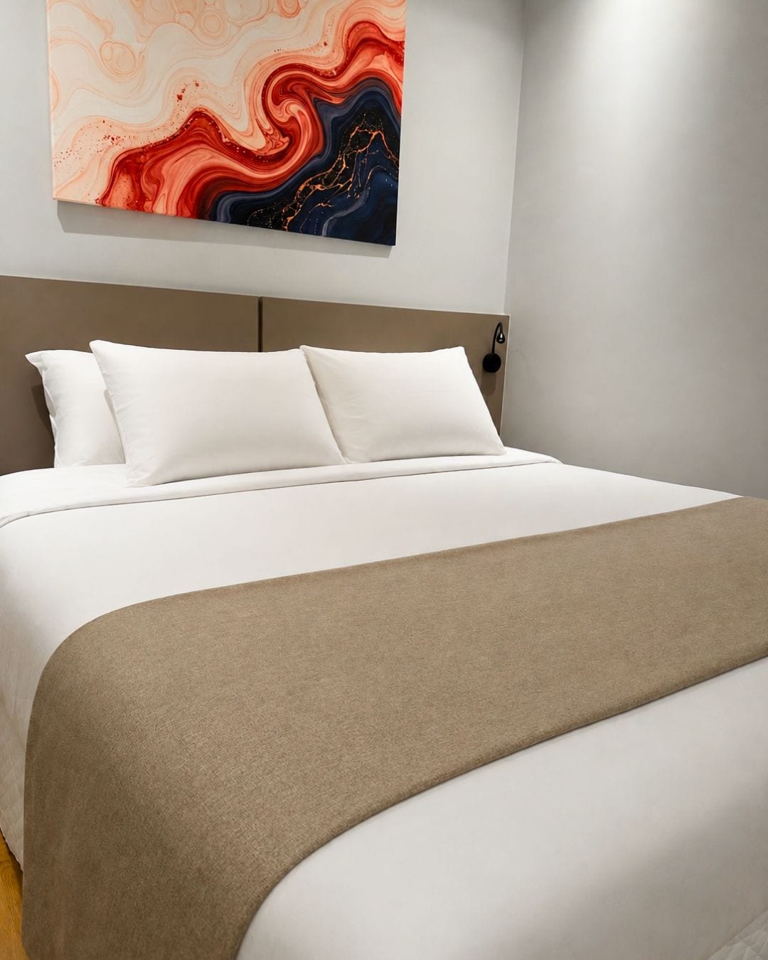 A modern bedroom with a bed, white bedding, a beige throw blanket, and a colorful abstract painting above the bed.