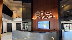 Un mostrador de recepción de hotel con una pantalla digital, una pared de madera con el nombre del hotel y vista al vestíbulo.