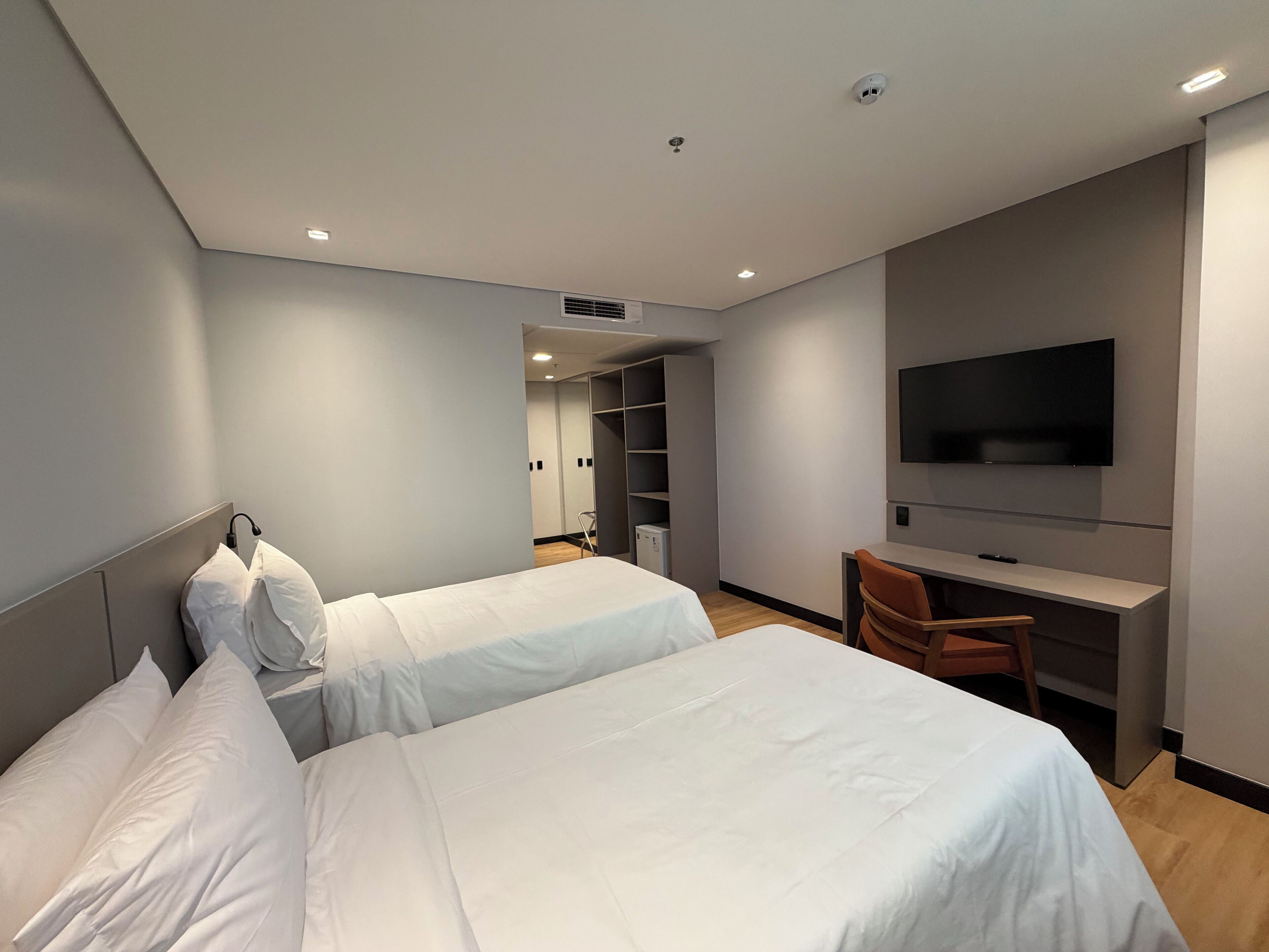 A hotel room with two beds, a desk with a chair, a TV, and a walk-in closet.