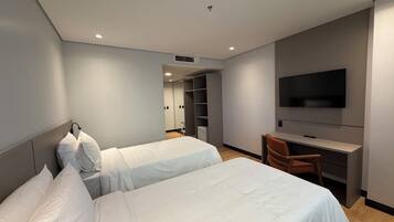 A hotel room with two beds, a desk with a chair, a TV, and a walk-in closet.
