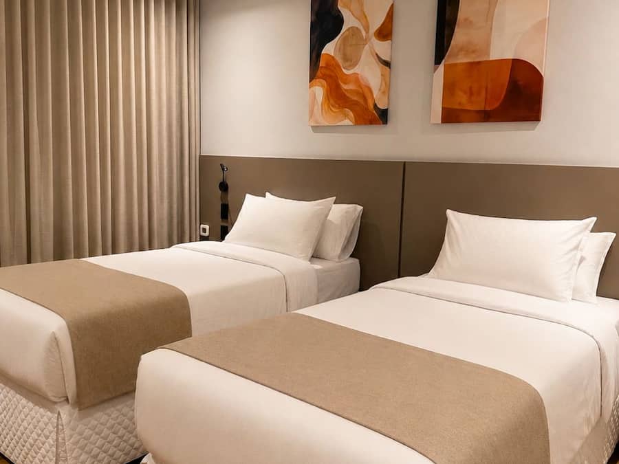 Quarto de hotel com duas camas, cabeceira e arte abstrata na parede.