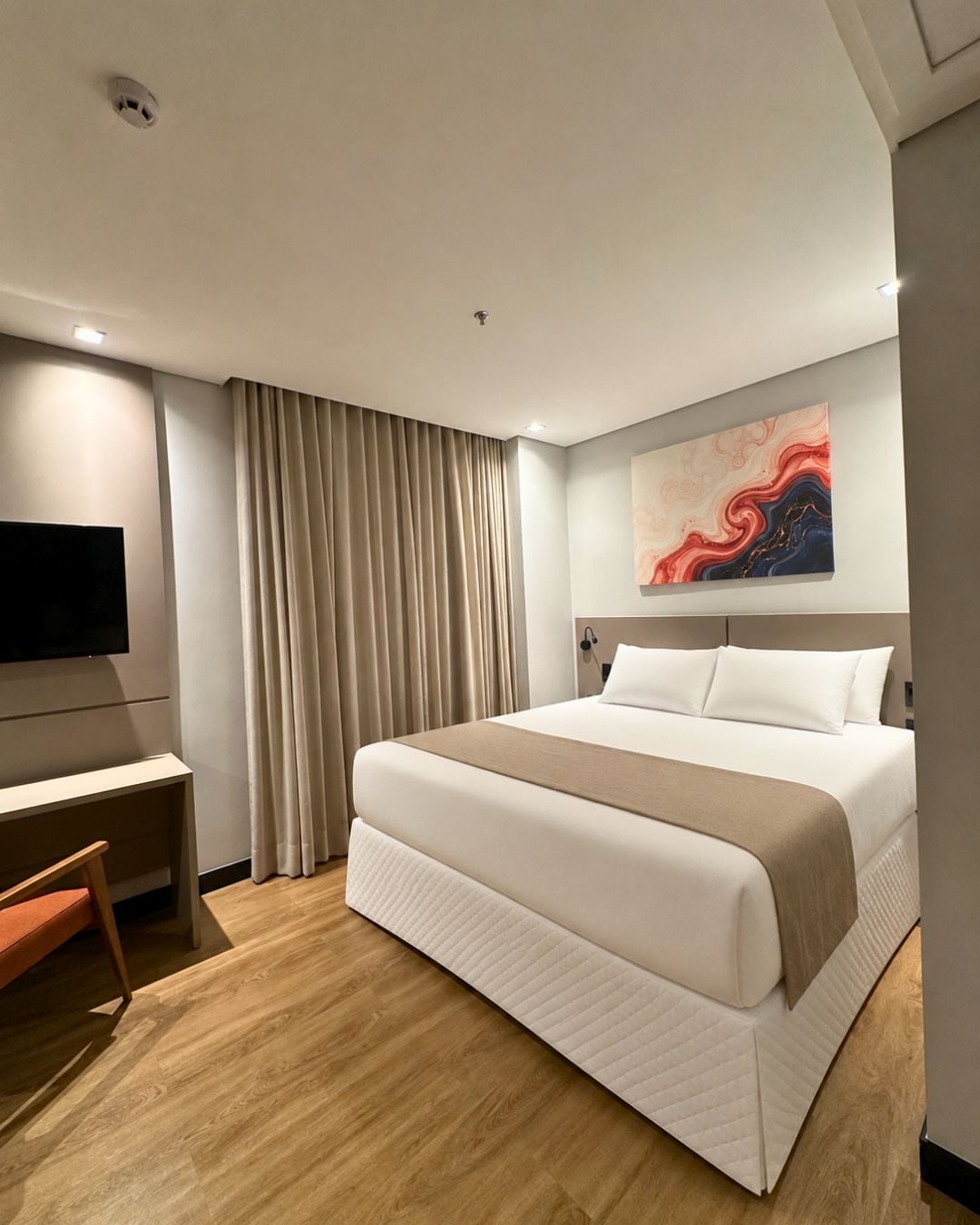 Une chambre d’hôtel avec un lit, un bureau, une chaise, une télévision et un tableau au mur.