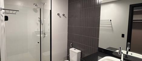 Une salle de bain moderne avec une douche à parois de verre, des toilettes blanches, un grand miroir et un plan de toilette noir.