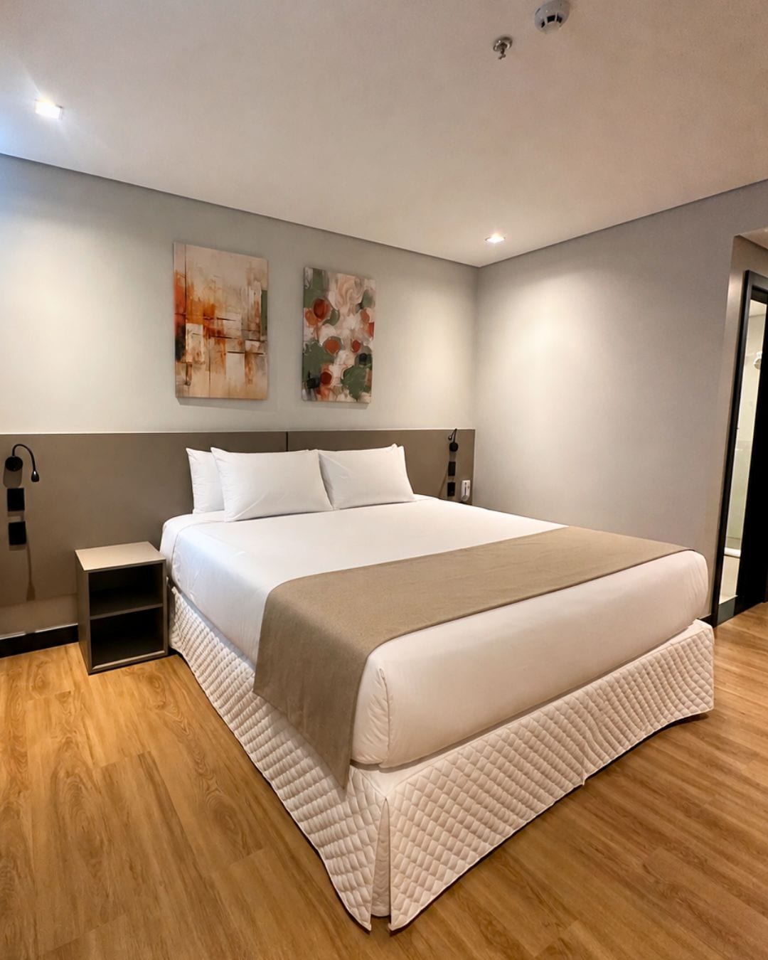 A modern bedroom with a large bed, bedside tables, and abstract wall art.