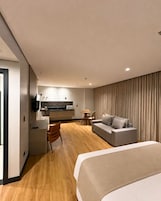 Una habitación de hotel moderna con una cama grande, un sofá, una zona de comedor y una kitchenette.