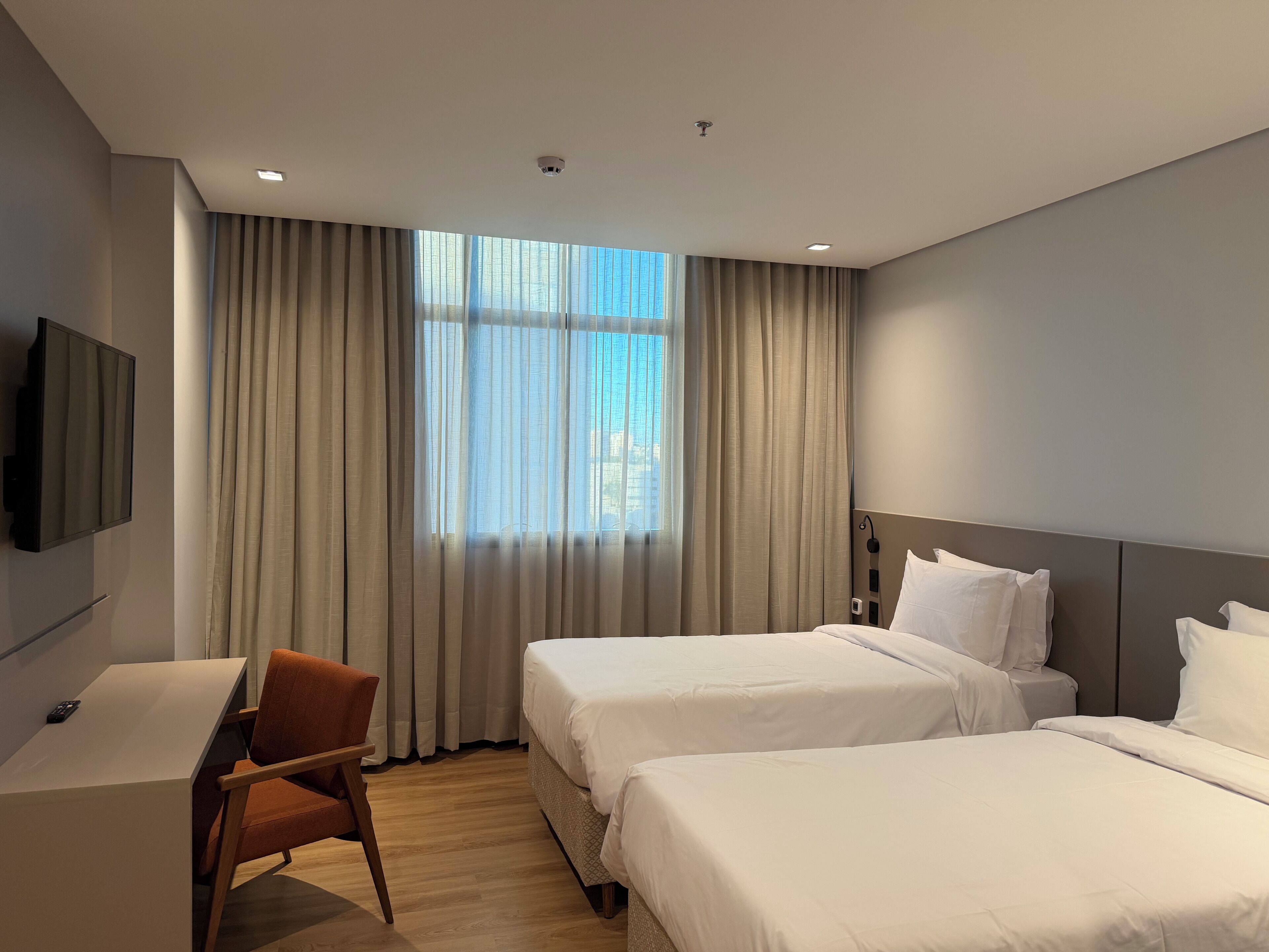 A hotel room with two beds, a desk, a chair, and a TV.