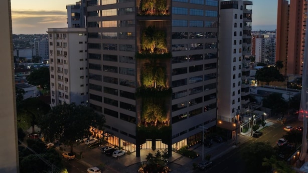 Un hotel de varios pisos con un jardín vertical, múltiples balcones y una vista despejada del entorno urbano.