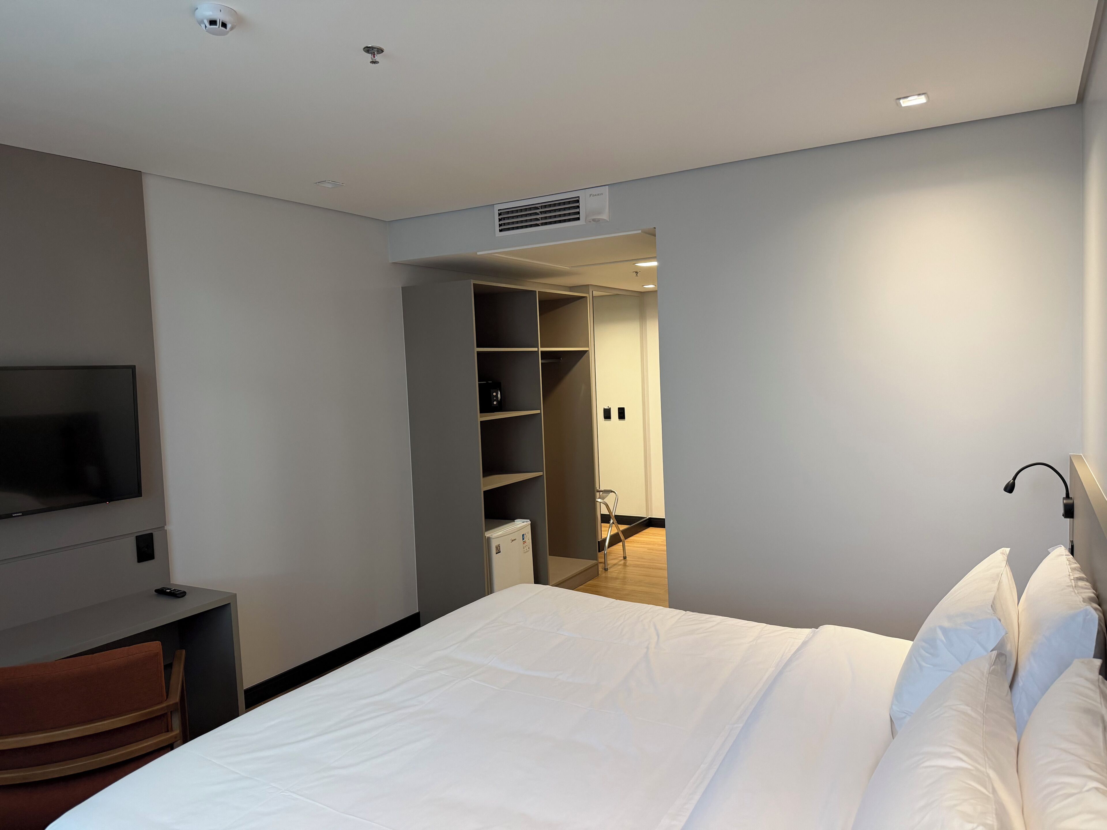 A modern hotel room with a bed, a TV, a desk, and a walk-in closet.