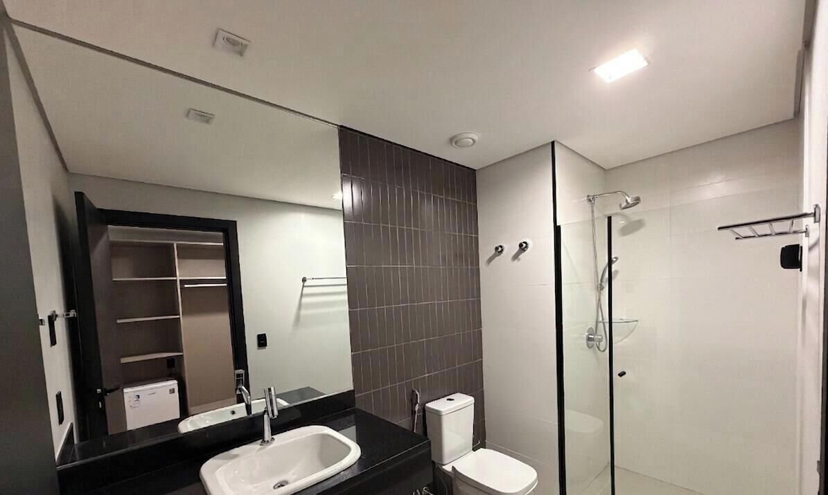 Un baño moderno con un espejo grande, lavamanos, inodoro y ducha con mampara de vidrio.