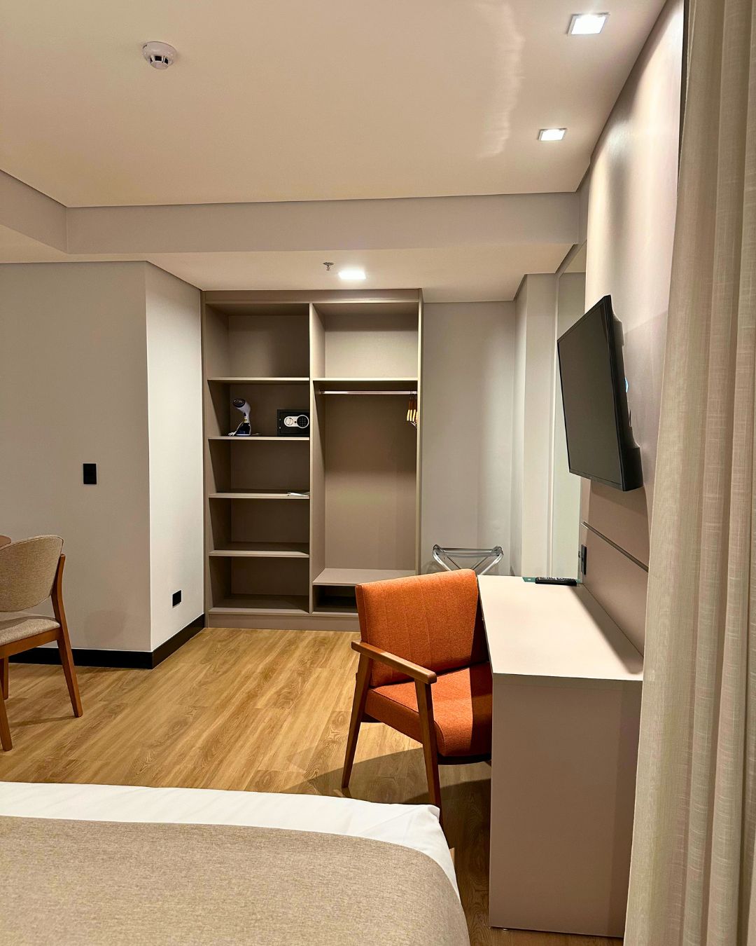 Habitación de hotel moderna con cama, escritorio, silla, televisor y estanterías empotradas.
