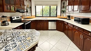 Una cocina con armarios de madera, un ventanal grande y un mantel estampado.