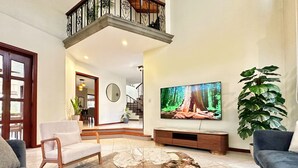 Una sala de estar con un televisor grande, un sofá, una mesa de centro y una escalera que sube a un nivel superior.