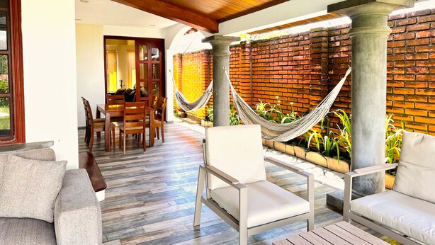 Un patio con techo de madera, pared de ladrillo, una hamaca y una mesa de comedor con sillas.